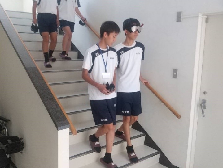 弱視体験で、1人が白内障体験のゴーグルをつけて見えにくい状態で、2人1組で階段を降りている様子。