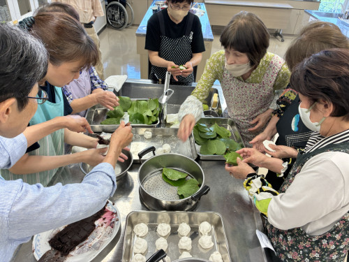 だんごを平たく伸ばし、こしあんを入れて、まきの葉で包んでいる様子。