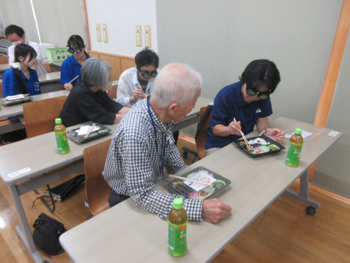 ペアになり弱視体験メガネをつけている相手に、昼食の中身を説明している参加者の様子